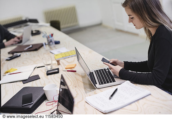 Young woman using smart phone at desk in creative office