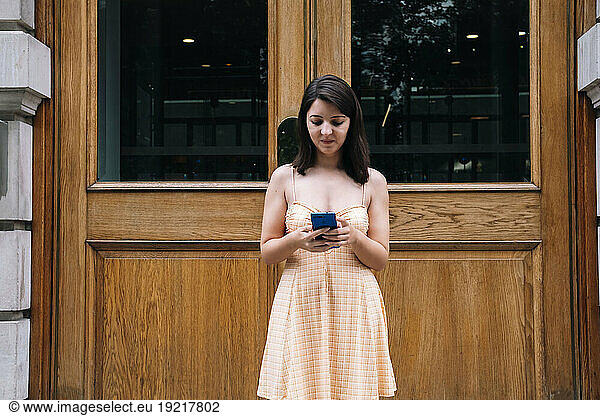 Young woman using smart phone in front of wooden door