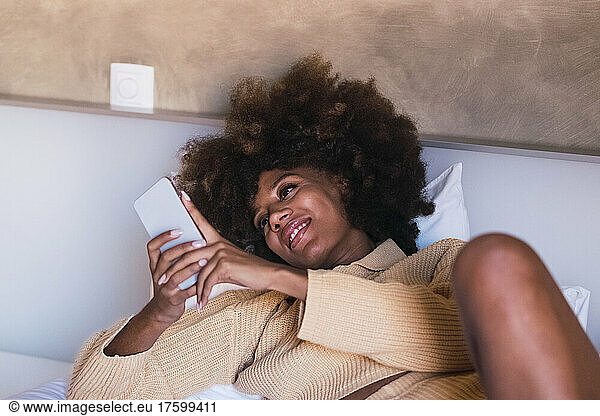 Young woman using smart phone lying on bed at home