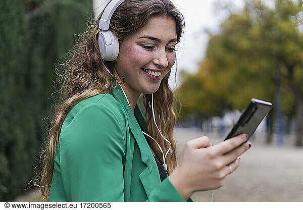 Young woman using smart phone while listening music through headphones in park
