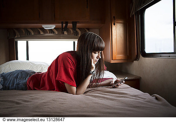 Young woman using smart phone while relaxing on bed in camper van