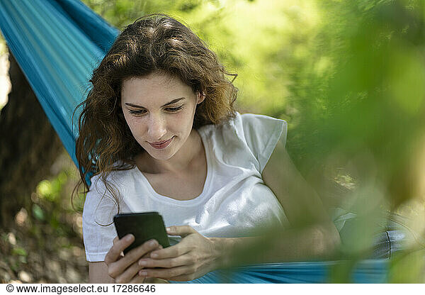 Young woman using smart phone while relaxing on hammock