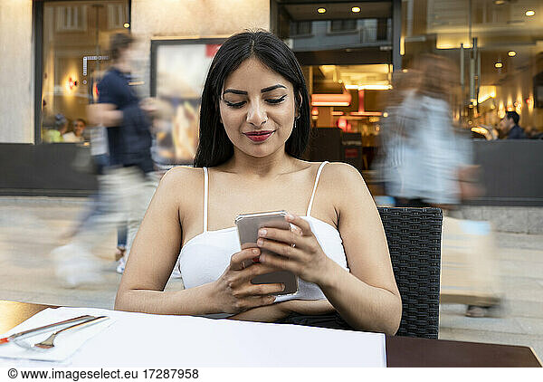 Young woman using smart phone while sitting at table in cafe