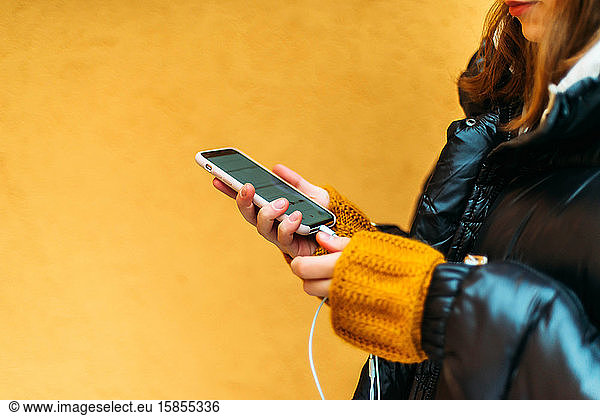 Young woman using smart phone while standing against yellow wall