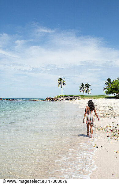 Young woman walking along beach shoreline in dress