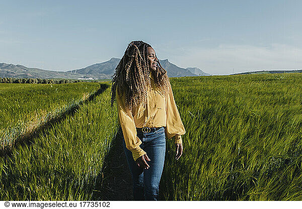 Young woman walking in meadow on sunny day