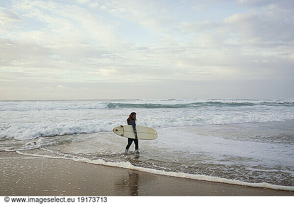 Young woman walking in sea with surfboard at beach