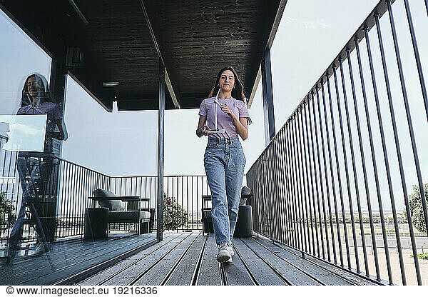 Young woman walking on balcony with model of wind turbine in hands
