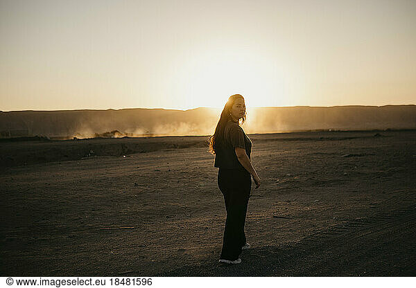 Young woman walking on dirt road at sunset