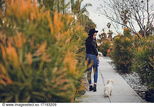 Young woman walking with her little dog on an urban setting.