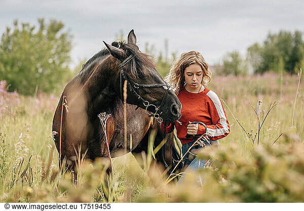 Young woman walks with horse across field  meadow.
