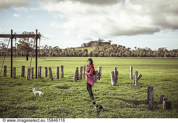 young woman walks with two small dogs through green farm land