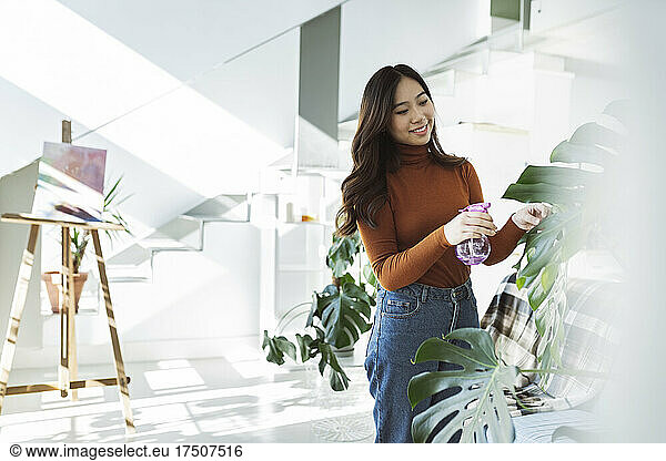 Young woman watering houseplant in living room
