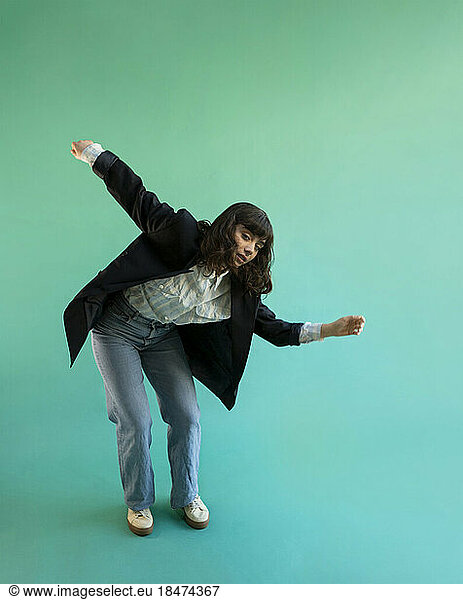 Young woman wearing blazer dancing against green background