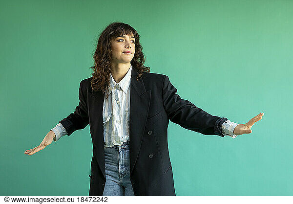 Young woman wearing blazer gesturing against green background