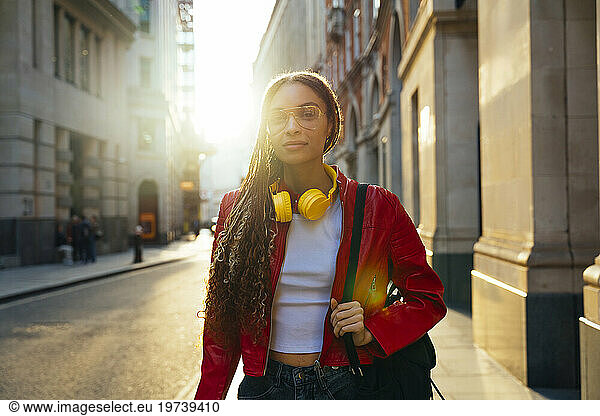 Young woman wearing eyeglasses and walking with backpack in city