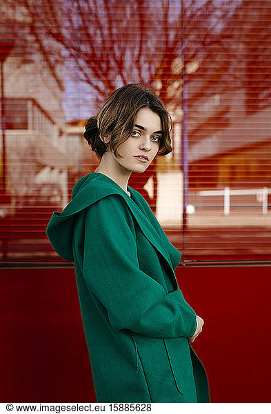 Young woman wearing green coat in front of a red glass pane