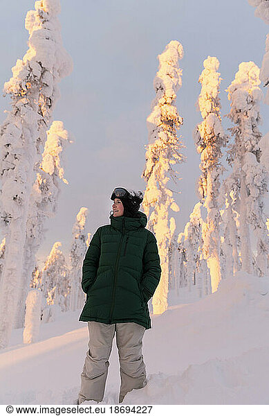 Young woman wearing green jacket standing in front of snow covered trees