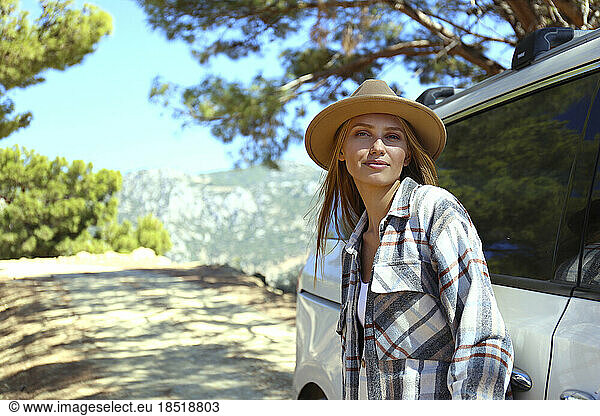 Young woman wearing hat leaning on car
