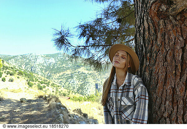 Young woman wearing hat relaxing on tree trunk