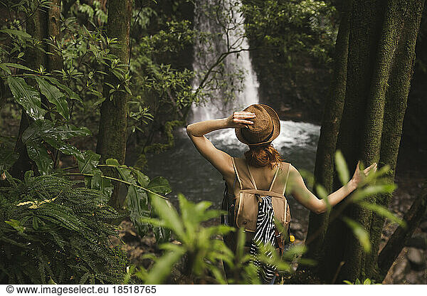 Young woman wearing hat standing in front of waterfall