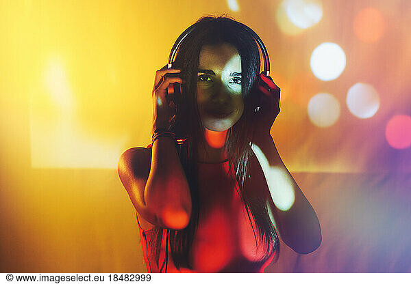 Young woman wearing headphone on illuminated colored background