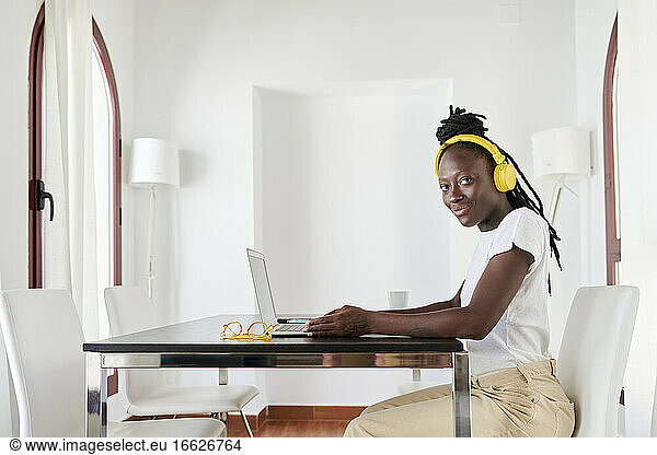Young woman wearing headphones using laptop on desk in home office