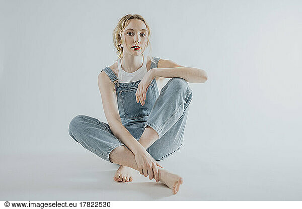 Young woman wearing overalls sitting against white background