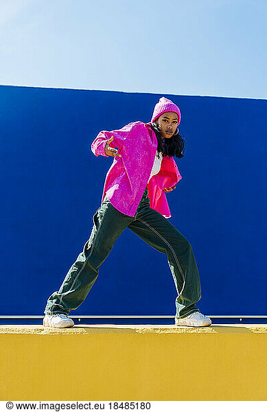 Young woman wearing pink jacket doing hip hop dance on wall