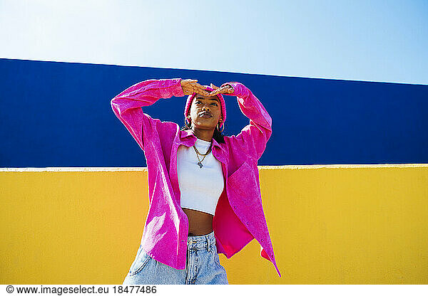 Young woman wearing pink jacket shielding eyes in front of wall