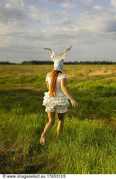 Young woman wearing rabbit costume running on grass field