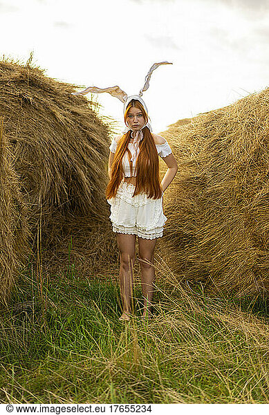Young woman wearing rabbit costume standing amidst hay bales