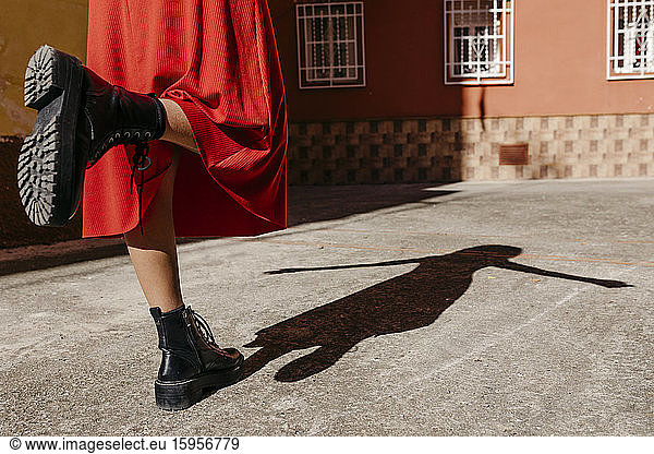 Young woman wearing red dress and black boots  playing with her shadow on the floor