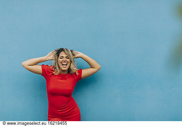 Young woman wearing red dress dancing against blue wall