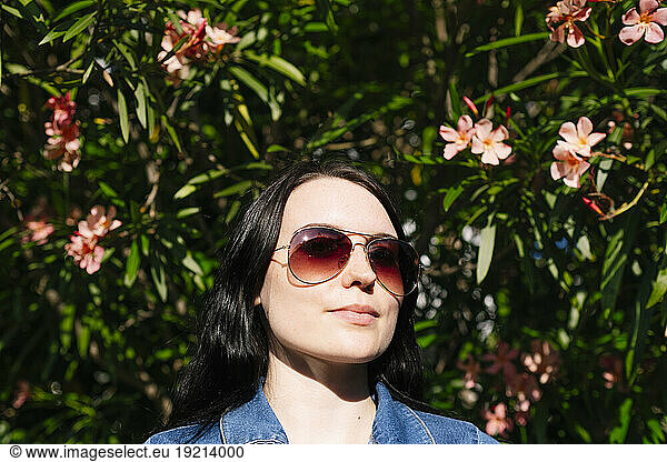 Young woman wearing sunglasses near flowering plants on sunny day