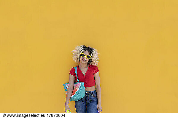 Young woman wearing sunglasses standing in front of yellow wall