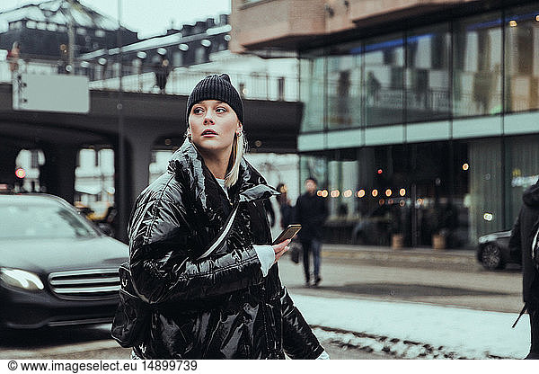 Young woman wearing warm clothing while looking away on street in city during winter
