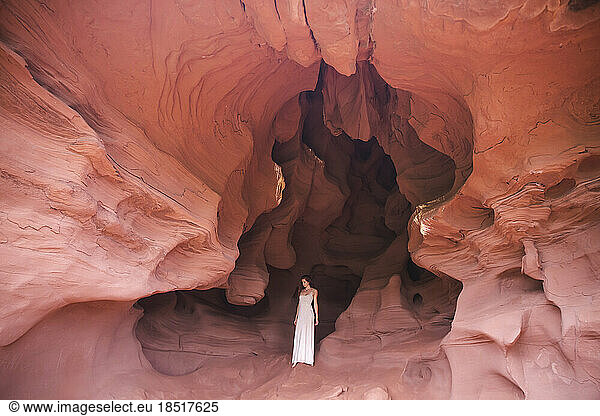 Young woman wearing white dress standing in red cave