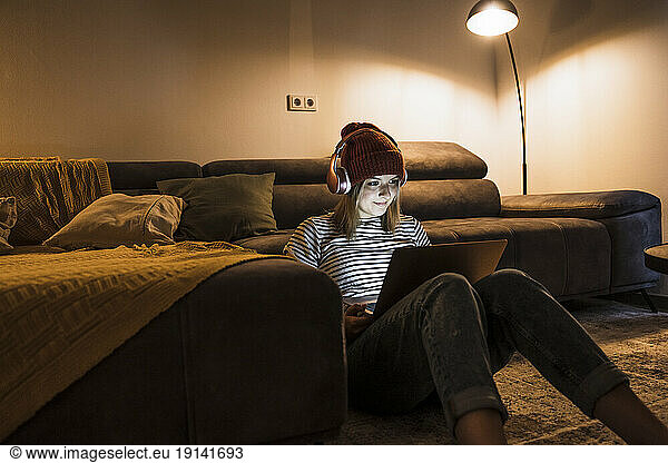 Young woman wearing wireless headphones and using laptop in living room