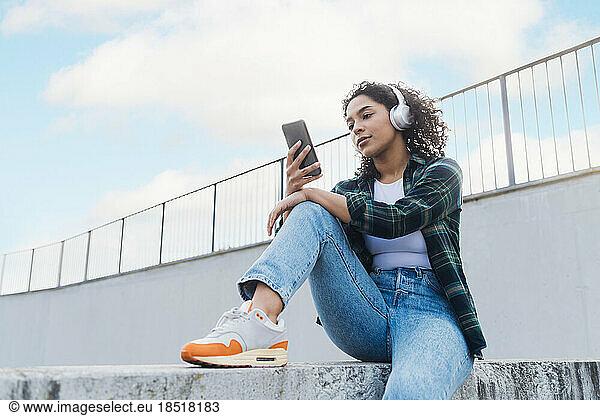 Young woman wearing wireless headphones using smart phone