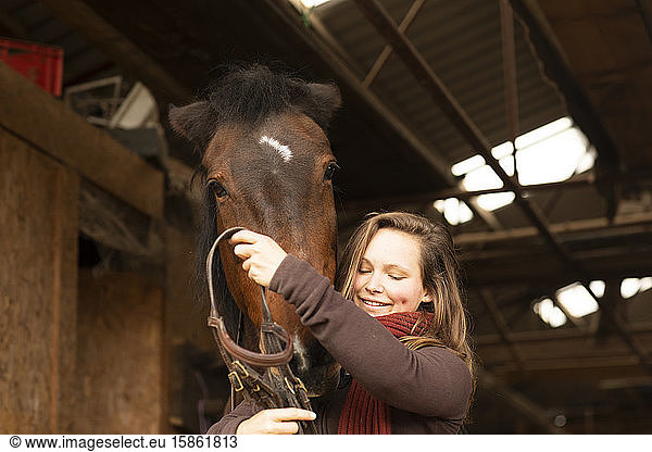 young woman with a horse in a horse stable with bridles