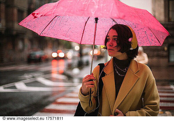 Young woman with an umbrella standing on street in city in autumn