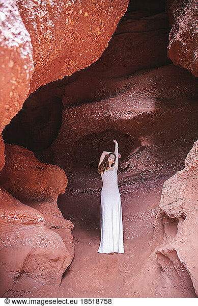 Young woman with arm raised standing in red cave
