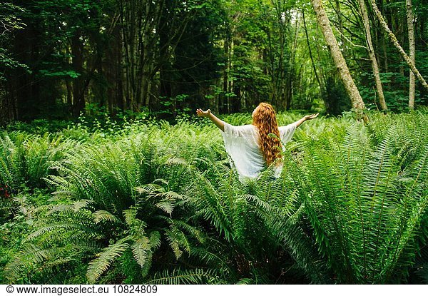 Young woman with arms open amongst forest ferns