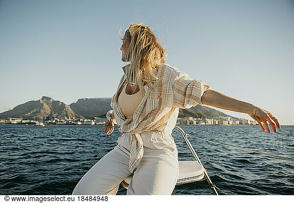 Young woman with arms outstretched on boat in front of clear sky