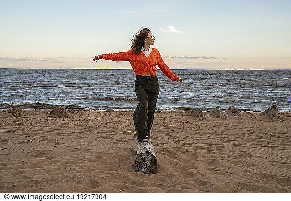 Young woman with arms outstretched walking on wooden log at beach