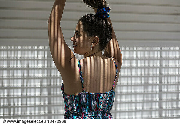 Young woman with arms raised facing wall