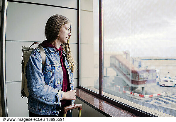 Young woman with backpack looking out of airport window