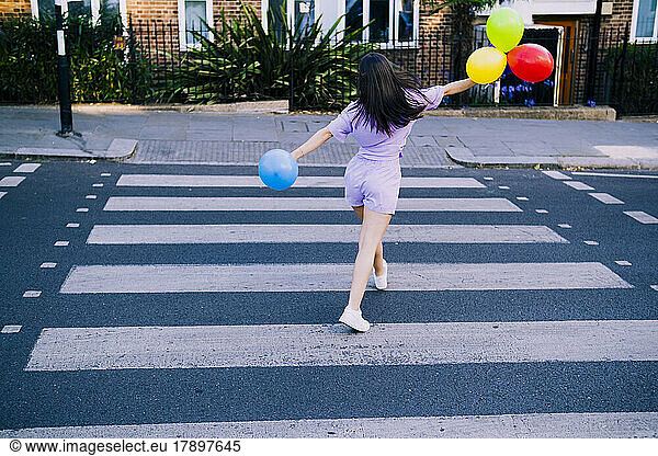 Young woman with balloons crossing city street