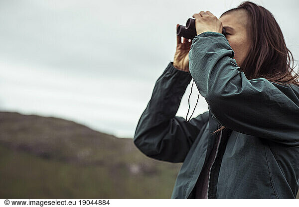 Young woman with binoculars looks for birds in Scotland